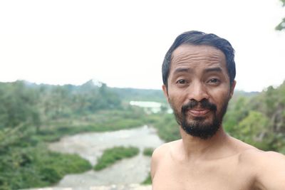 Portrait of shirtless man smiling against mountains