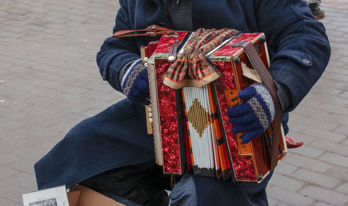 Close-up of a man's hand playing button accordion outdoors in winter.
