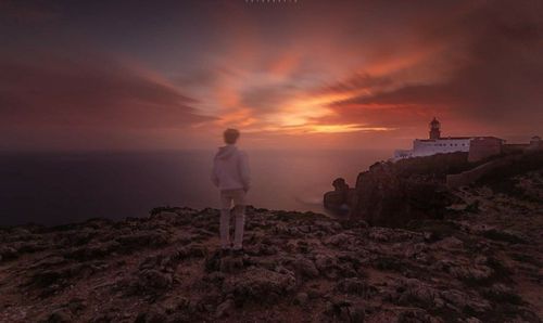 Woman standing on rock by sea against sky during sunset