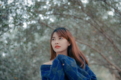 Portrait of a beautiful young woman standing against trees