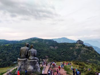 Statue of people on mountain against cloudy sky
