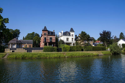 Houses by lake and buildings against clear blue sky