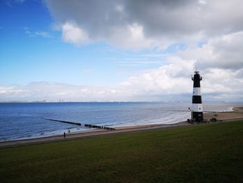 Lighthouse amidst sea and buildings against sky