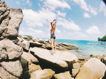 Man standing on rock by sea against sky