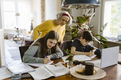 Senior woman assisting grandchildren doing homework while sitting at home