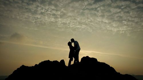 Low angle view of silhouette couple kissing against sky during sunset