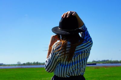 Rear view of woman standing on field against clear blue sky