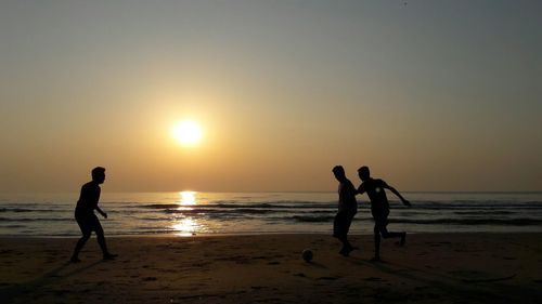 People playing volleyball at beach during sunset