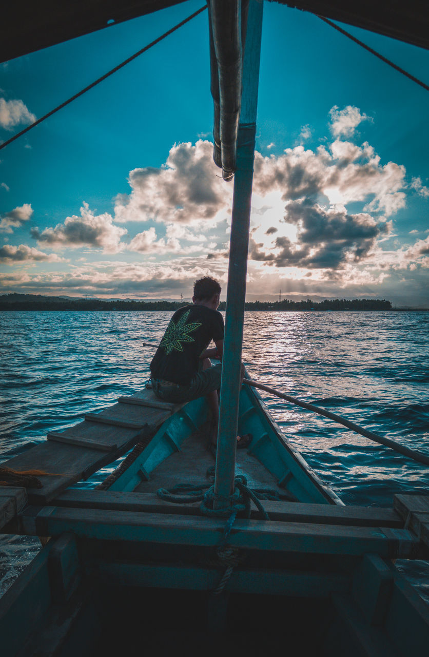 MAN SITTING ON BOAT AGAINST SEA