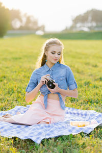 Young woman holds a camera in her hands in the summer outdoors, sitting on a blanket person