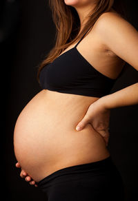 Midsection of woman touching hair over black background