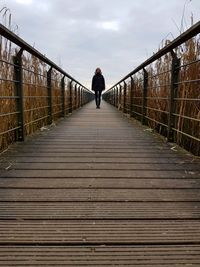 Walking on footbridge against sky