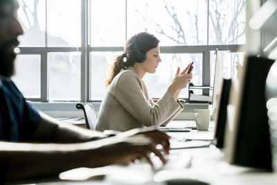 Businesswoman using smart phone while sitting by colleague in office