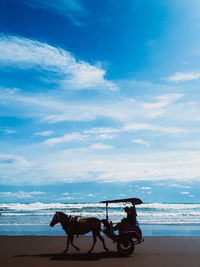 Horse riding horses at beach against sky