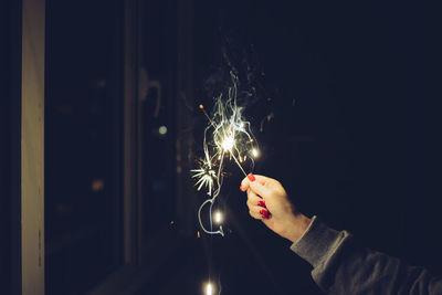 Close-up of woman hand holding illuminated sparkler at night