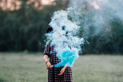 Young woman holding distress flare while standing on grassy field at park