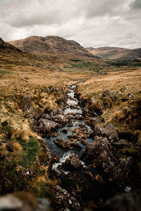 Scenic view of stream flowing through rocks against sky