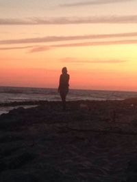 Rear view of silhouette man standing on beach against sky during sunset