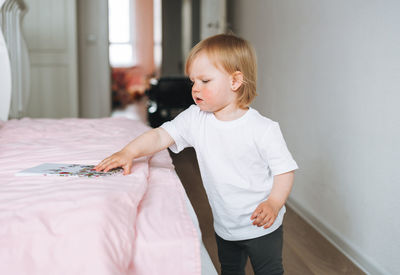 Cute funny baby girl in home clothes reading a book on bed at home