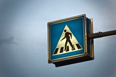 Low angle view of pedestrian crossing sign against sky
