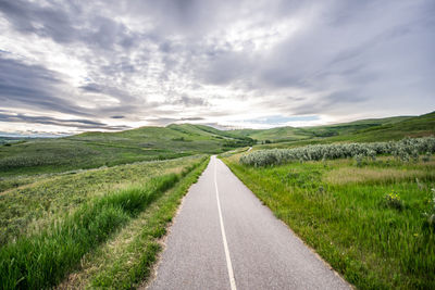 Empty road amidst field against sky