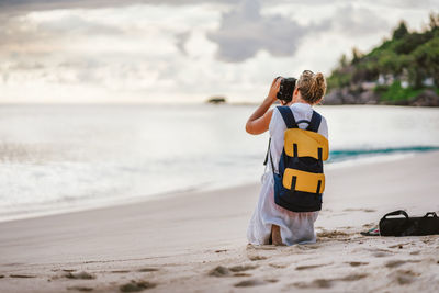 Rear view of woman photographing at beach