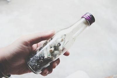 Cropped hand of person holding bottle with ash and cigarette butts