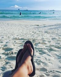 Low section of woman relaxing on beach against sky