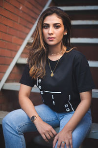 Portrait of beautiful young woman sitting against brick wall