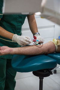 Unrecognizable crop medic with syringe collecting blood from arm of patient in medical clinic