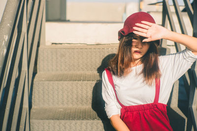 Young woman shielding eyes while sitting on staircase