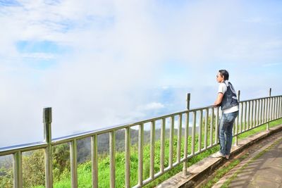 Man standing by railing against sky