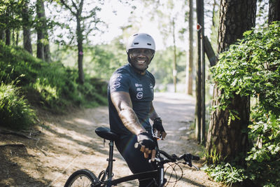 Portrait of smiling man leaning by cycle on footpath