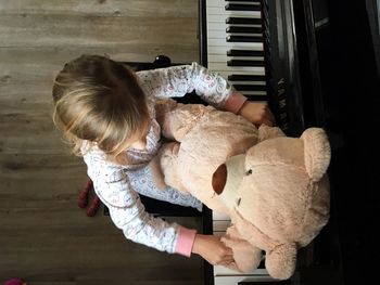 Directly above shot of girl with teddy bear playing piano at home