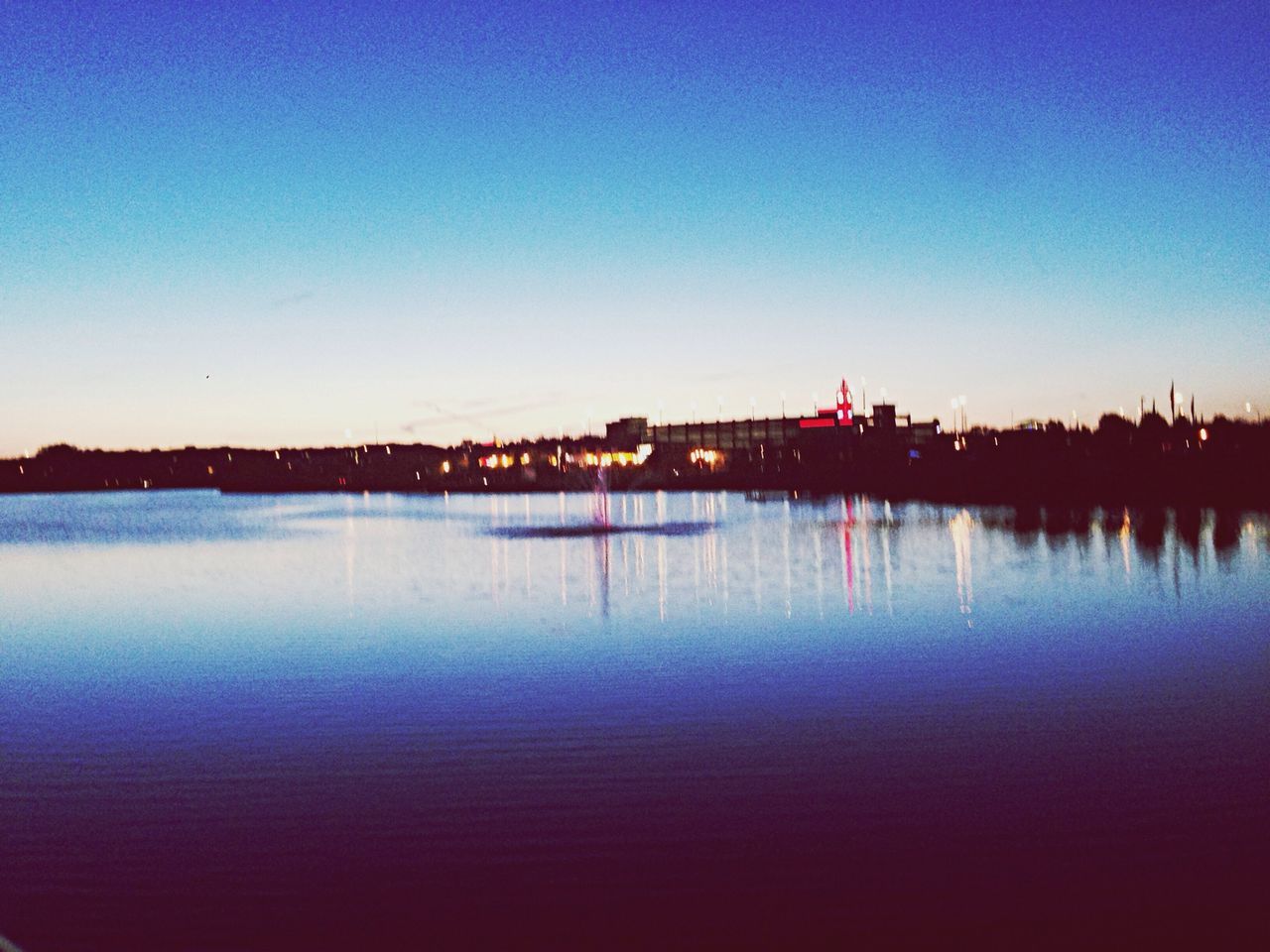 clear sky, water, copy space, waterfront, reflection, blue, tranquility, tranquil scene, lake, built structure, sunset, illuminated, scenics, architecture, dusk, building exterior, beauty in nature, river, nature, calm