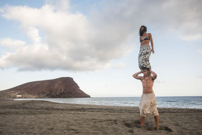 Low angle view of woman standing on shoulders of man against sky