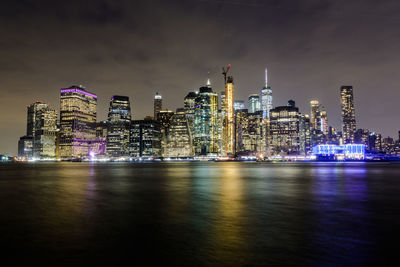 Illuminated buildings by river against sky at night