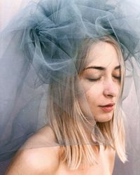 Close-up of shirtless woman wearing veil against wall