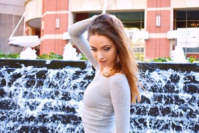 Side view of beautiful young woman standing against water fountain