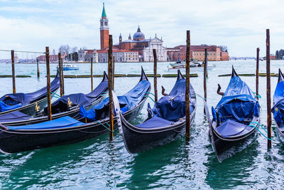 Boats moored in sea by buildings against sky