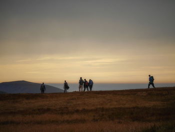 Silhouette people on field against sky during sunset