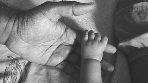 Cropped image of father and child holding hands on bed