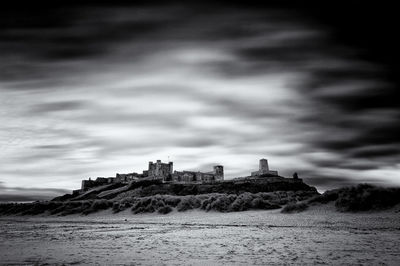 Bamburgh castle by sea against cloudy sky