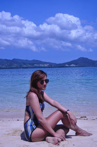 Young woman sitting on shore at beach against sky