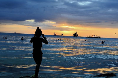 Silhouette woman standing on shore against sea during sunset
