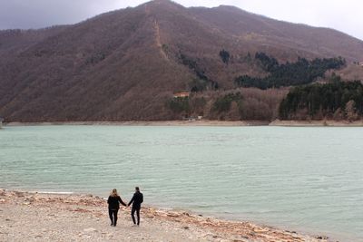 People on shore against mountains