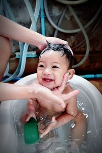 Cropped hands of mother touching baby boy taking bath in bathtub