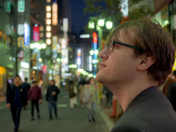 Close-up portrait of young man looking away in city at night