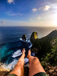 Low section of man relaxing on rock over sea against sky