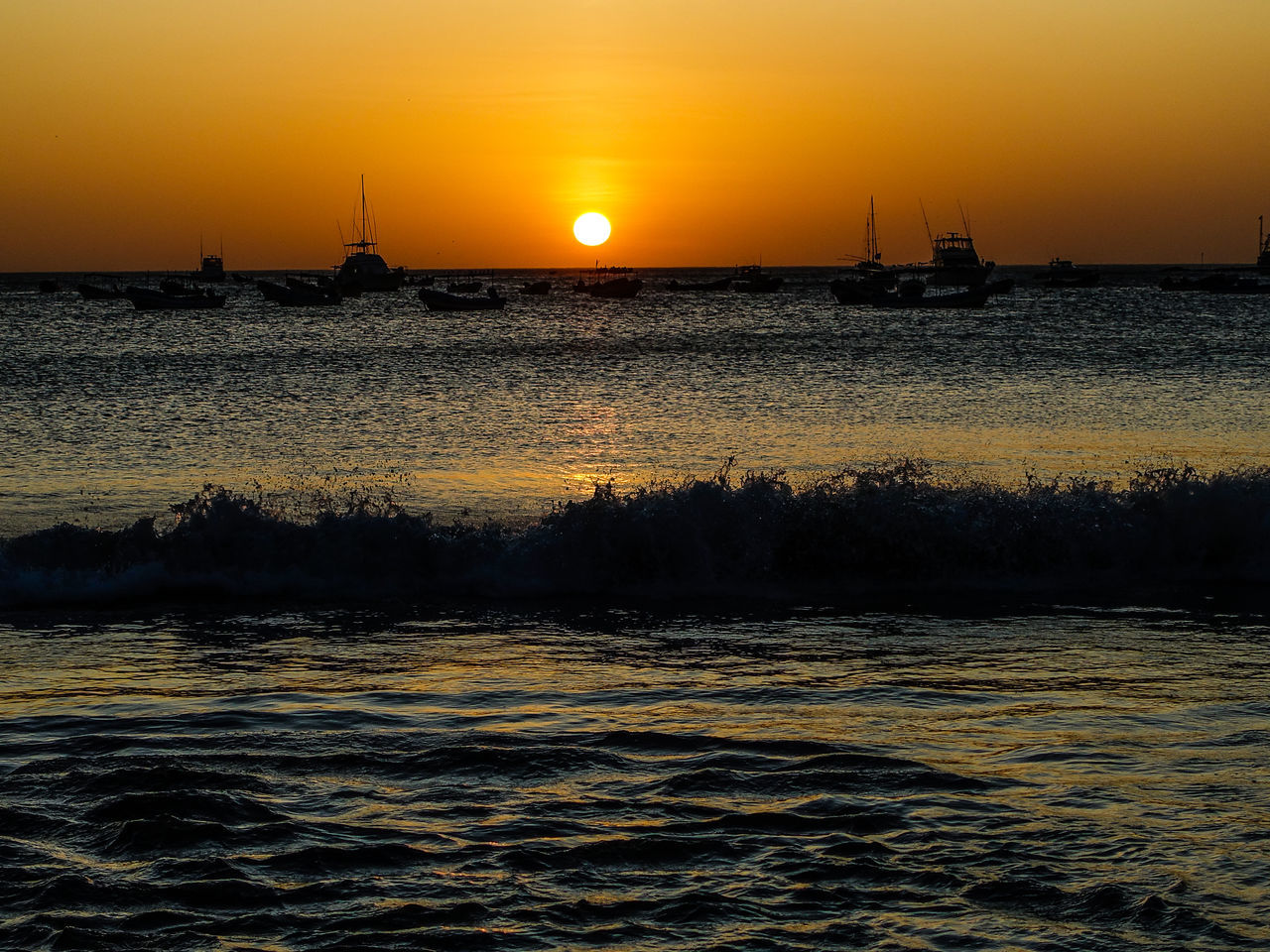 water, sunset, sky, sea, horizon, beauty in nature, scenics - nature, nature, nautical vessel, dawn, sun, ocean, transportation, shore, wave, orange color, silhouette, tranquility, afterglow, ship, tranquil scene, environment, sunlight, idyllic, evening, mode of transportation, coast, no people, reflection, travel, architecture, land, outdoors, horizon over water, travel destinations, seascape, dramatic sky, motion, landscape, beach, urban skyline, non-urban scene, sailing, cloud, sailboat